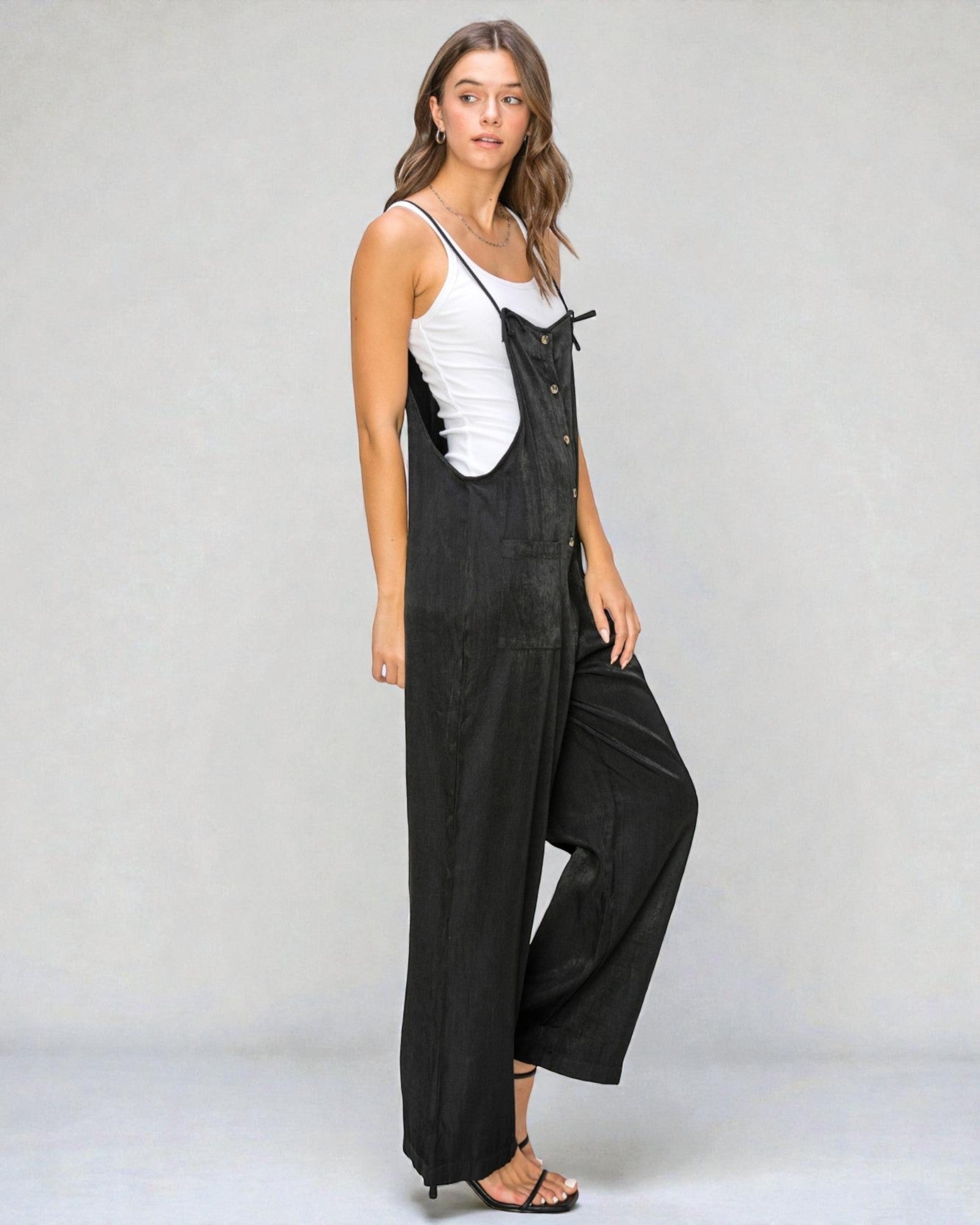 Woman wearing black overalls with a white top on a plain background