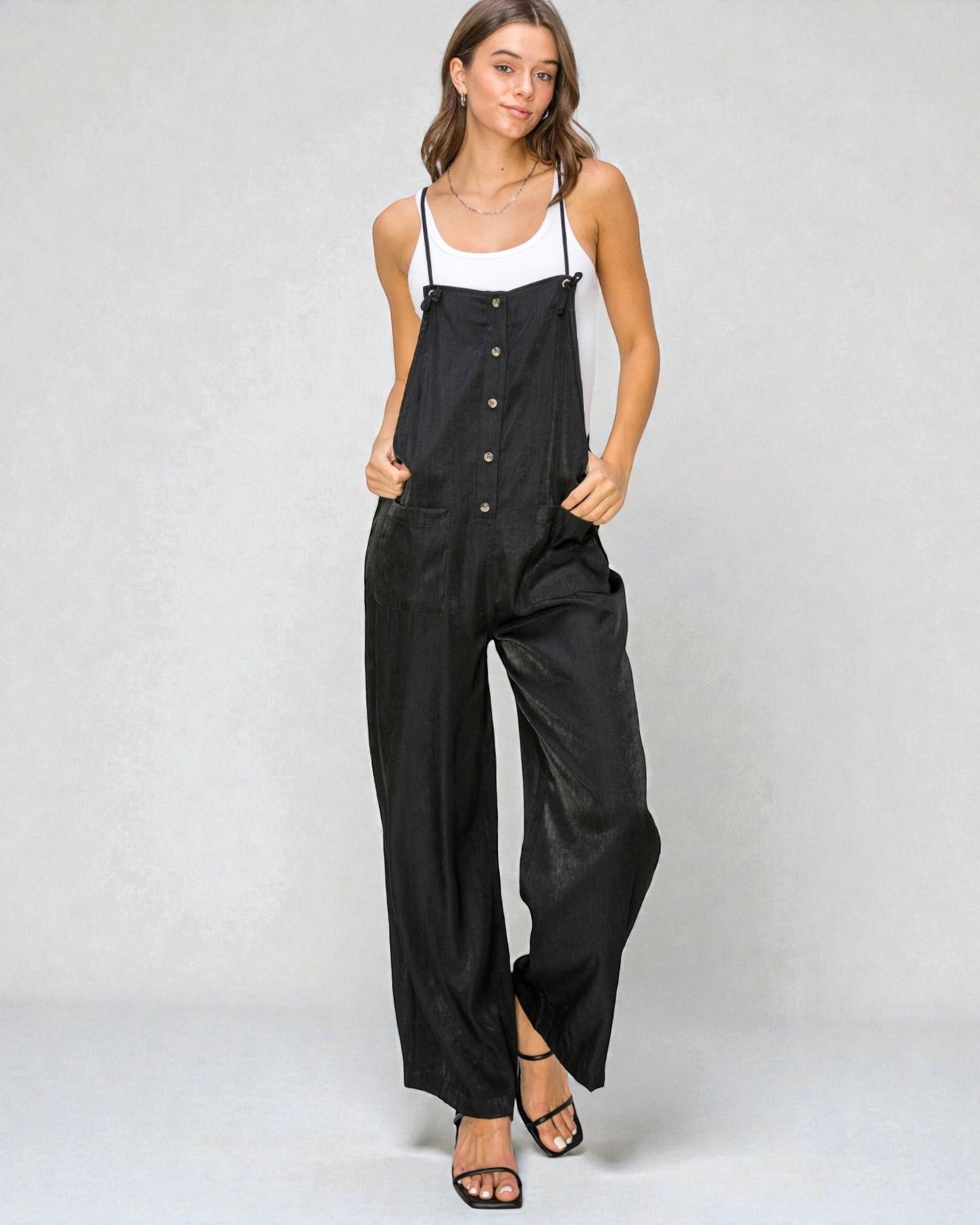 Woman wearing a black jumpsuit with a white top on a plain background