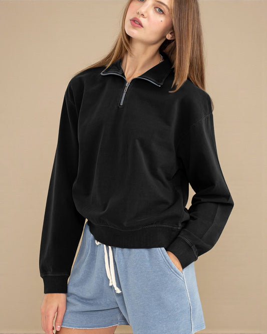 Woman wearing a black zip-up sweatshirt and blue shorts on a beige background