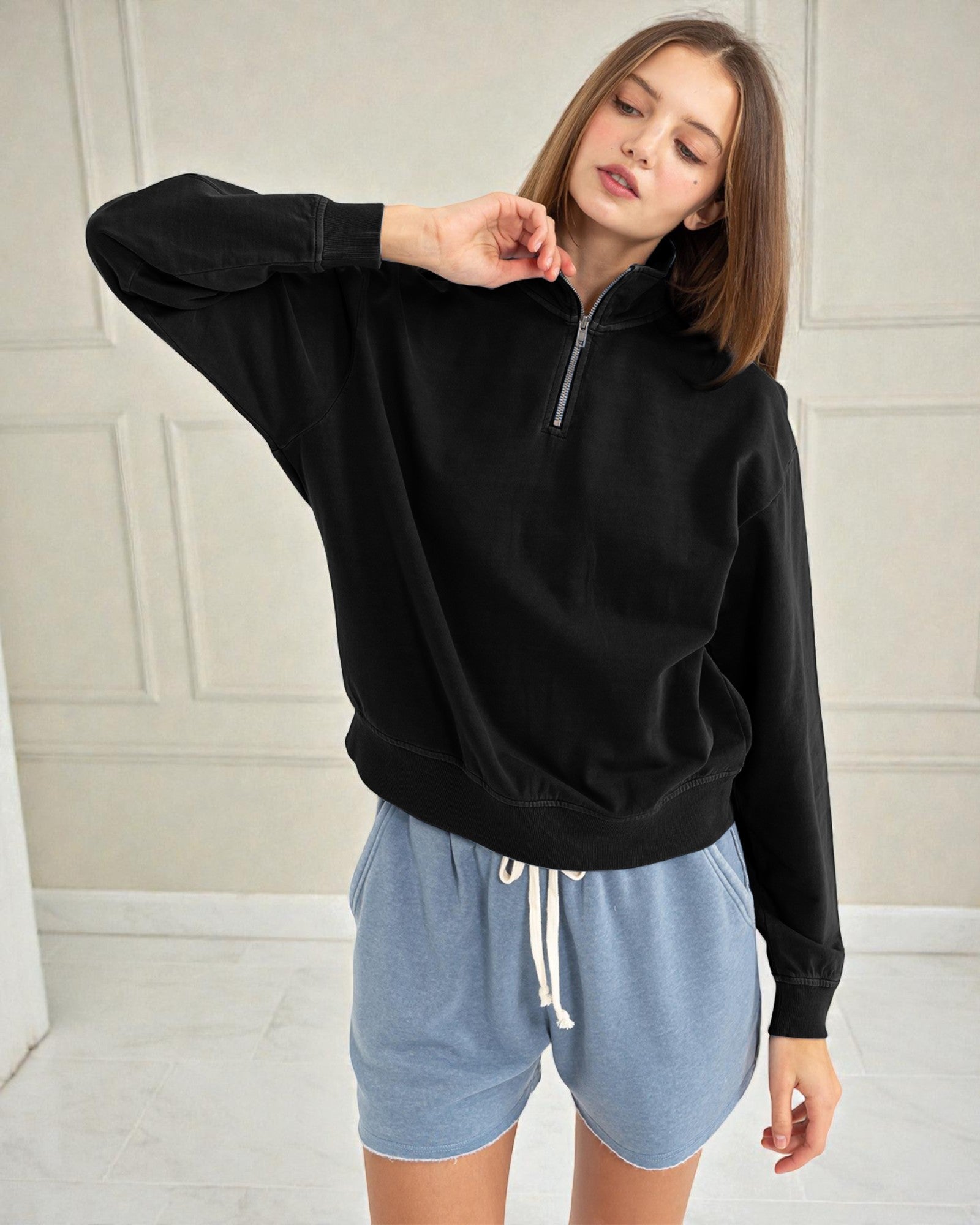 Woman wearing a black hoodie and blue shorts against a neutral background