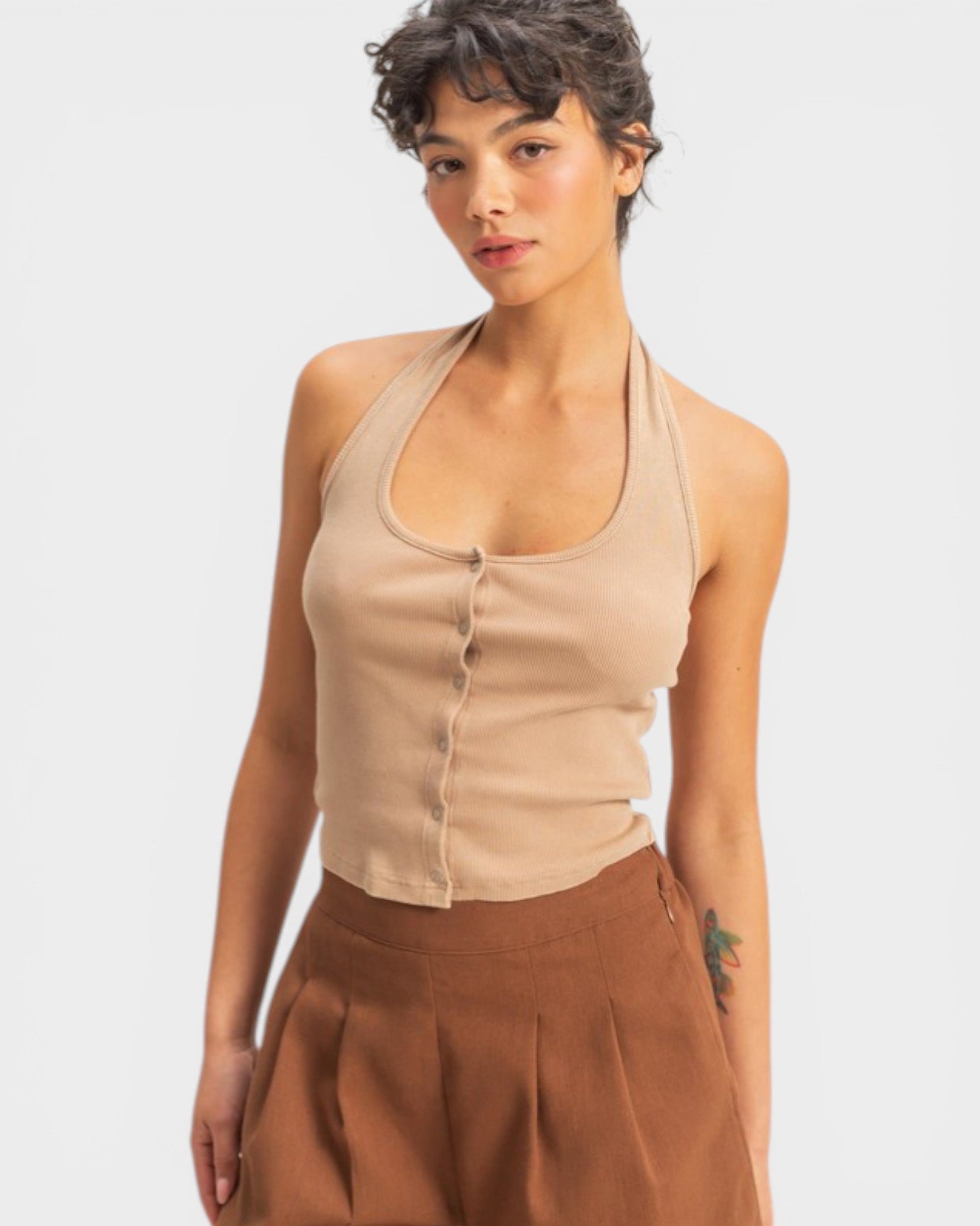 Woman wearing a beige halter top and brown pants on a white background