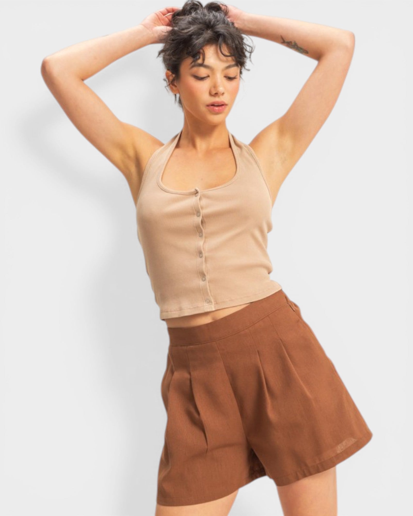 Woman wearing a beige tank top and brown shorts against a white background