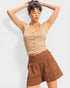Woman wearing a beige tank top and brown shorts against a white background