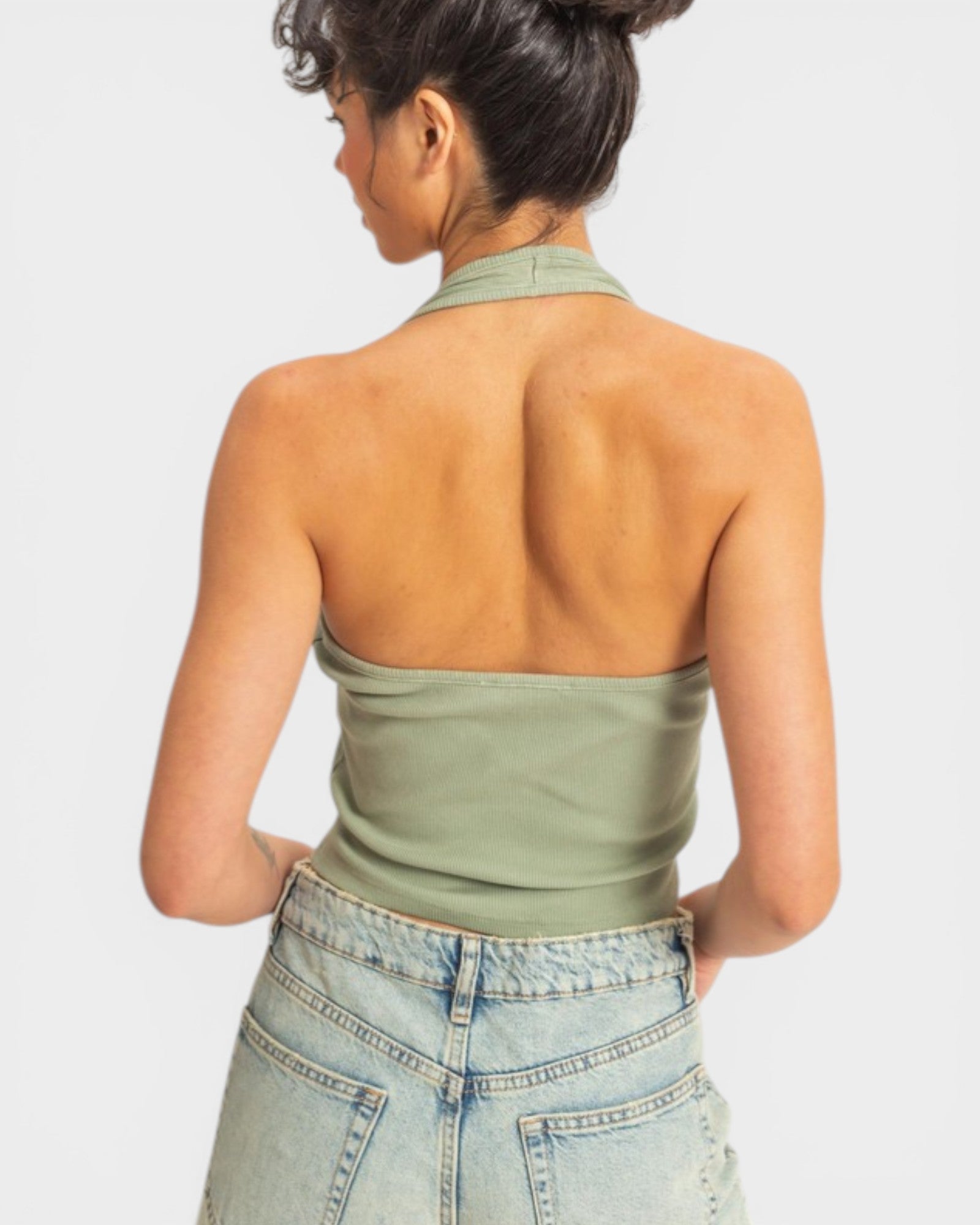 Woman wearing a green halter top and light blue jeans on a white background