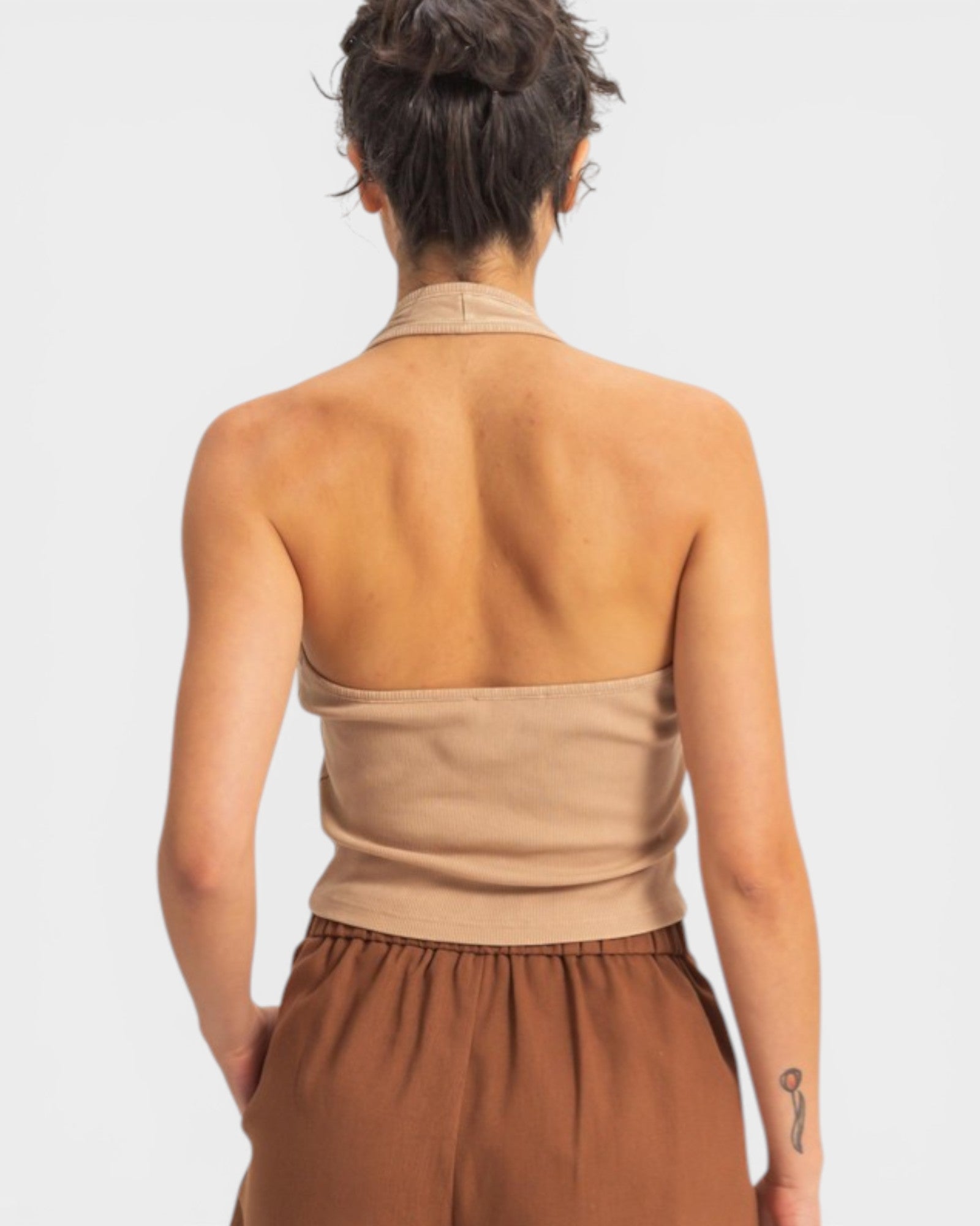 Person wearing a beige halter top and brown pants on a light gray background