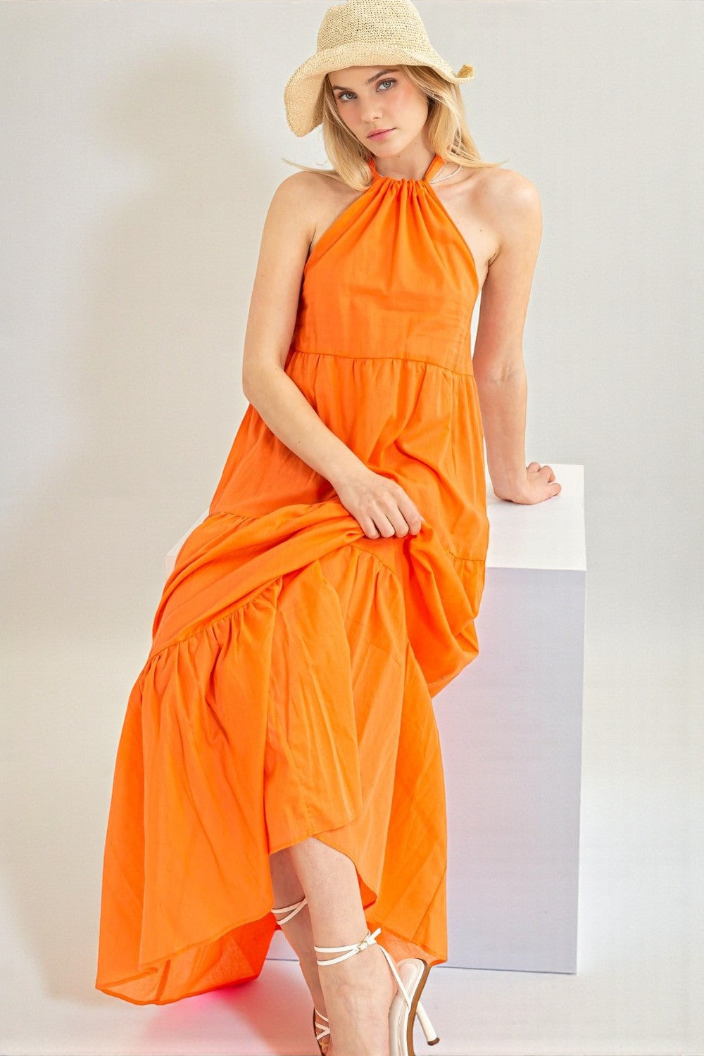Woman wearing an orange halter neck dress and beige hat on a white background