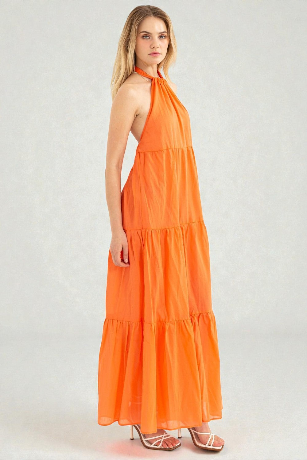 Woman wearing an orange halter neck dress on a white background