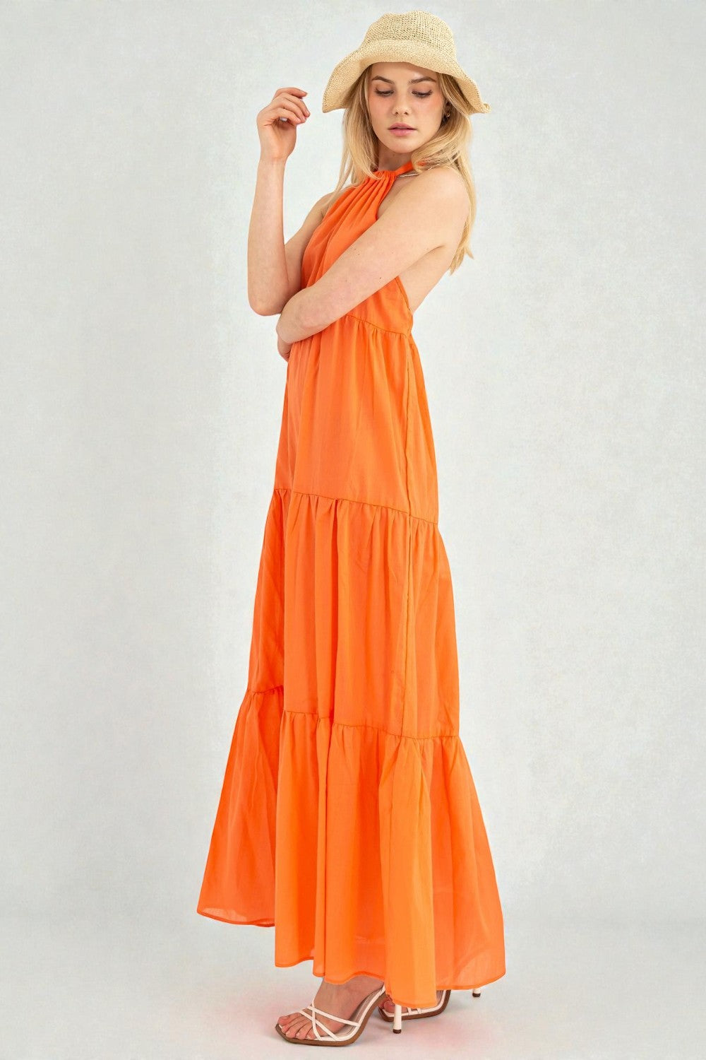 Woman wearing an orange tiered dress and straw hat on a white background