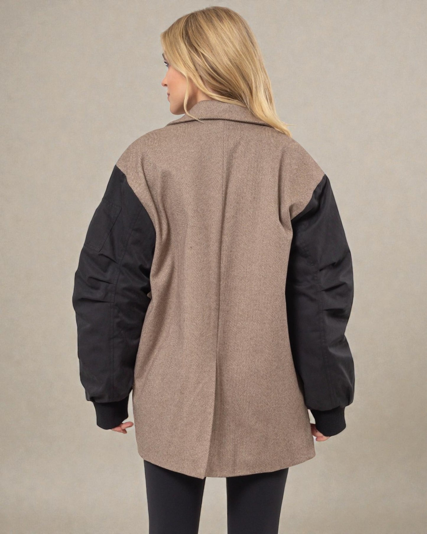 Woman wearing a two-tone coat with beige back and black sleeves on a plain background