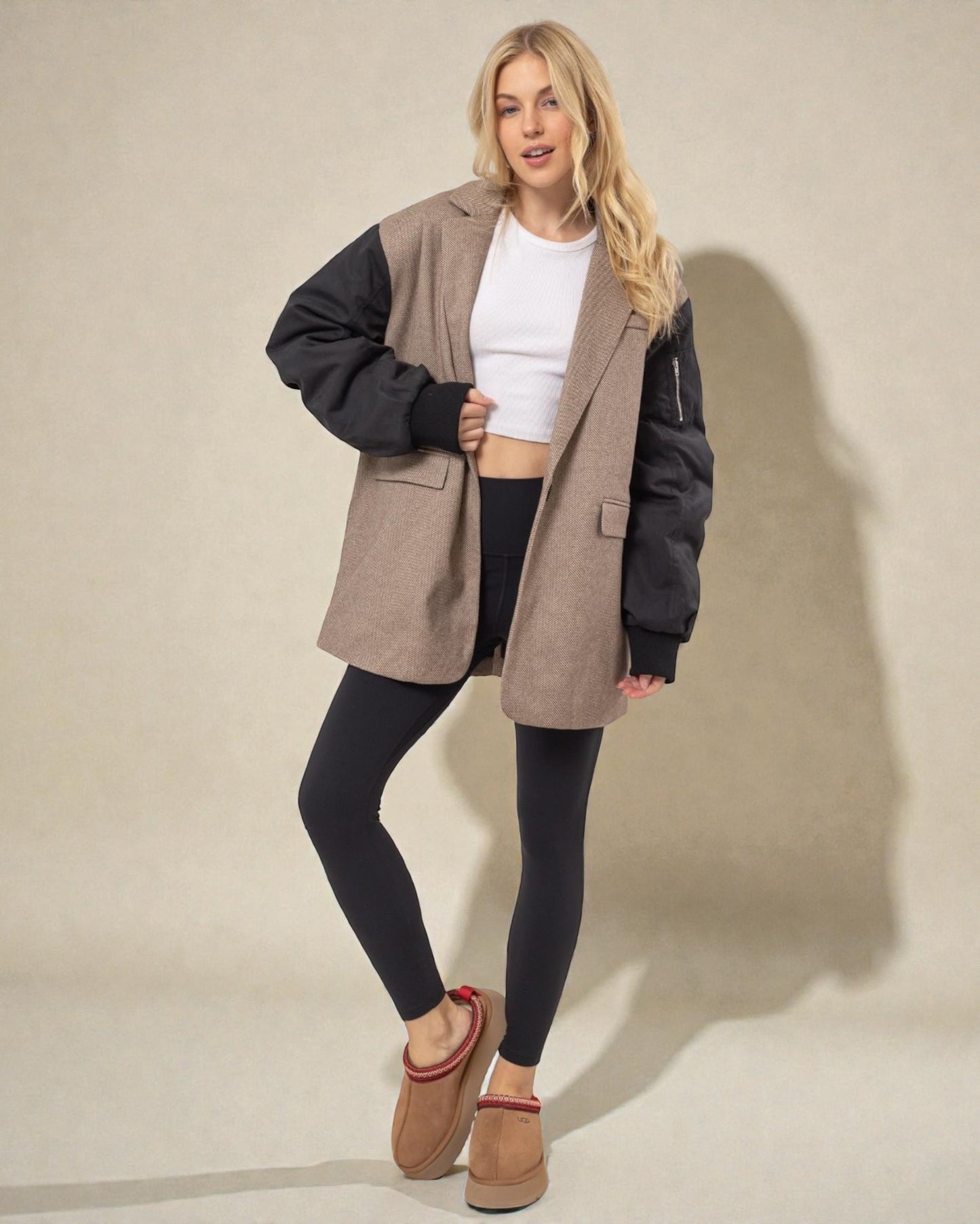 Woman wearing a beige and black jacket with black leggings on a beige background