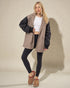 Woman wearing a beige and black jacket with black leggings on a beige background