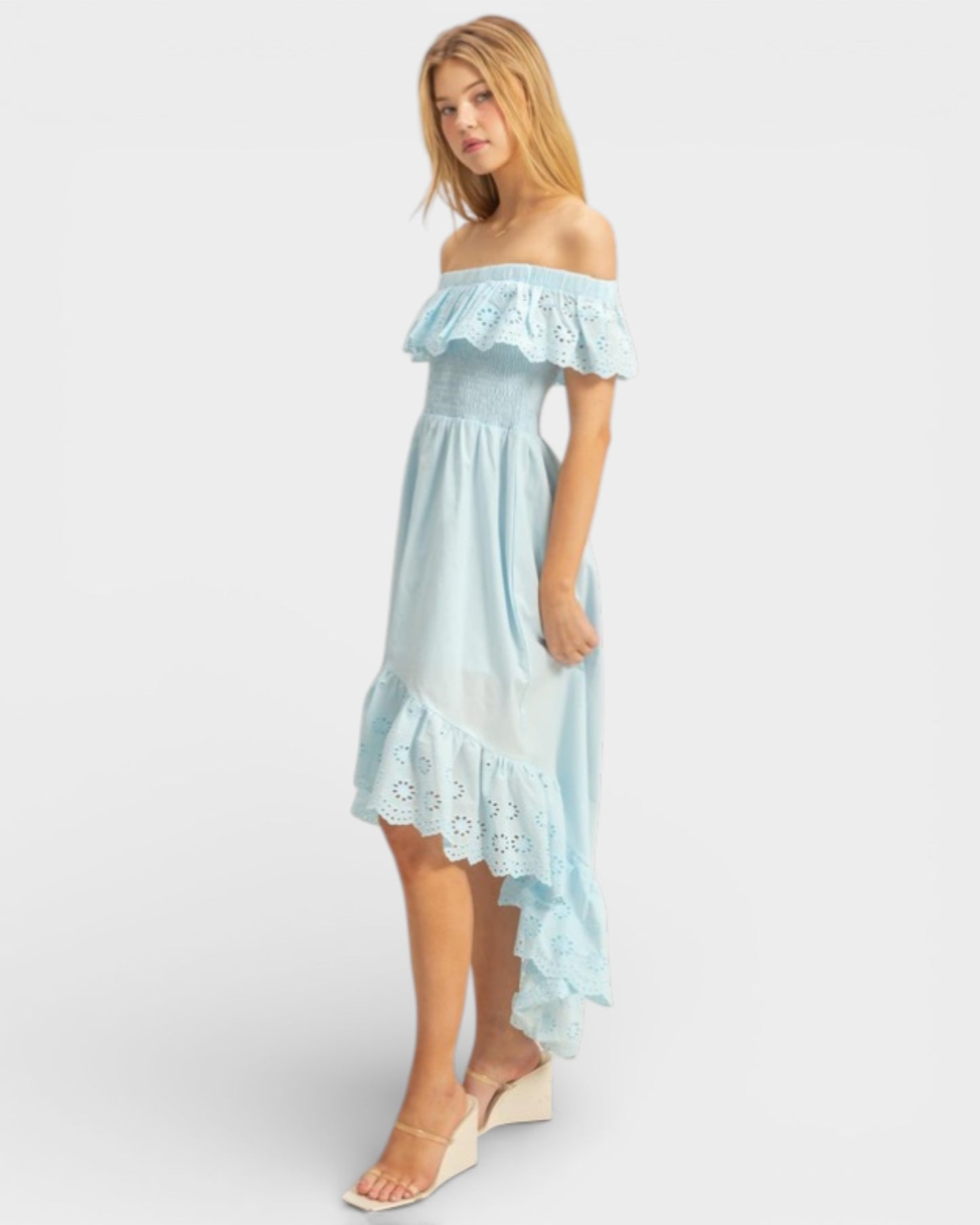 Woman wearing a light blue off-shoulder dress with ruffled details on a white background