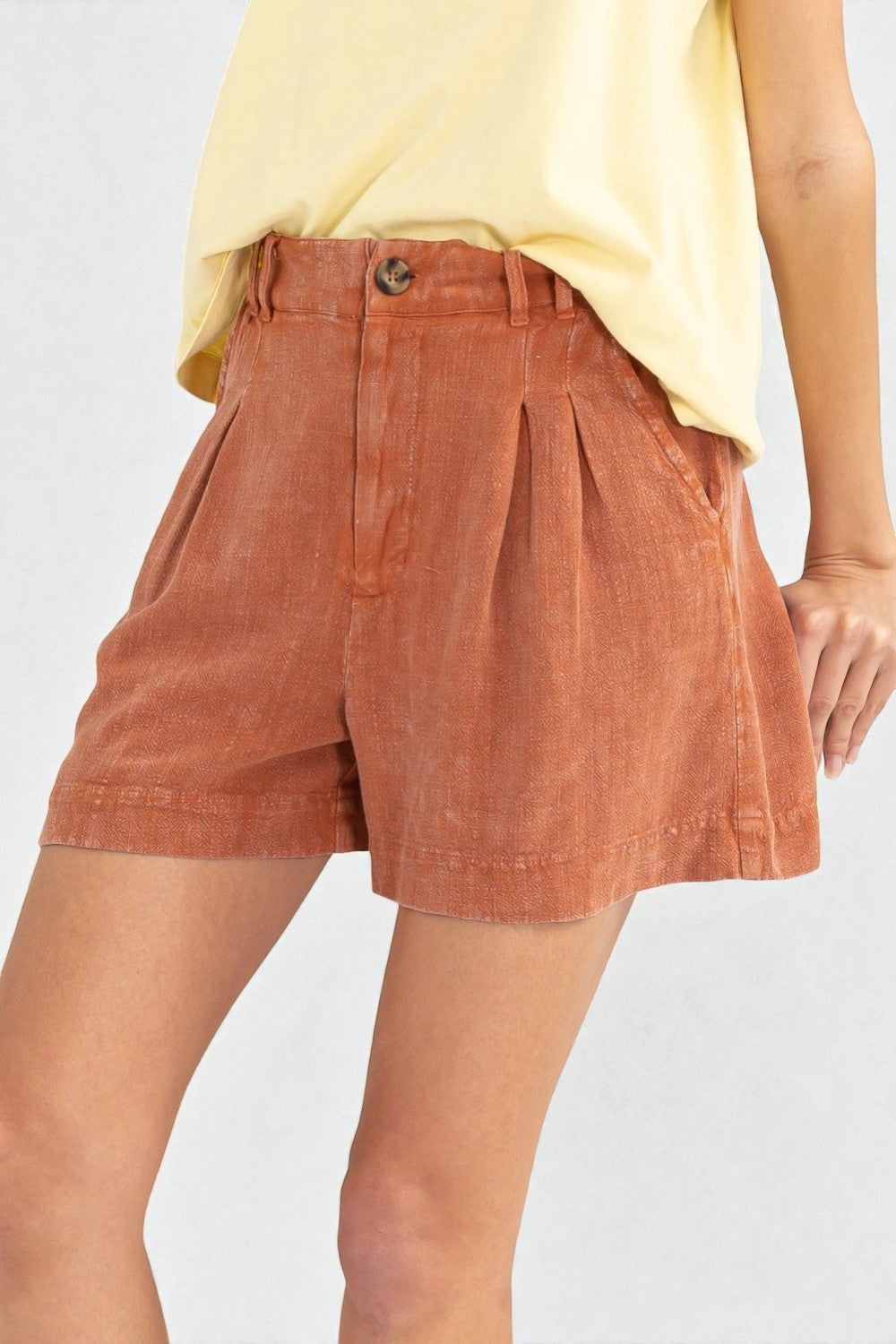 Person wearing rust-colored shorts and a yellow top on a light gray background