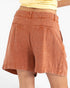 Rust-orange linen shorts shown from the back on a model, featuring a relaxed fit, belt loops, and two back welt pockets.