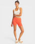 Woman wearing a white sleeveless top and orange shorts on a light gray background