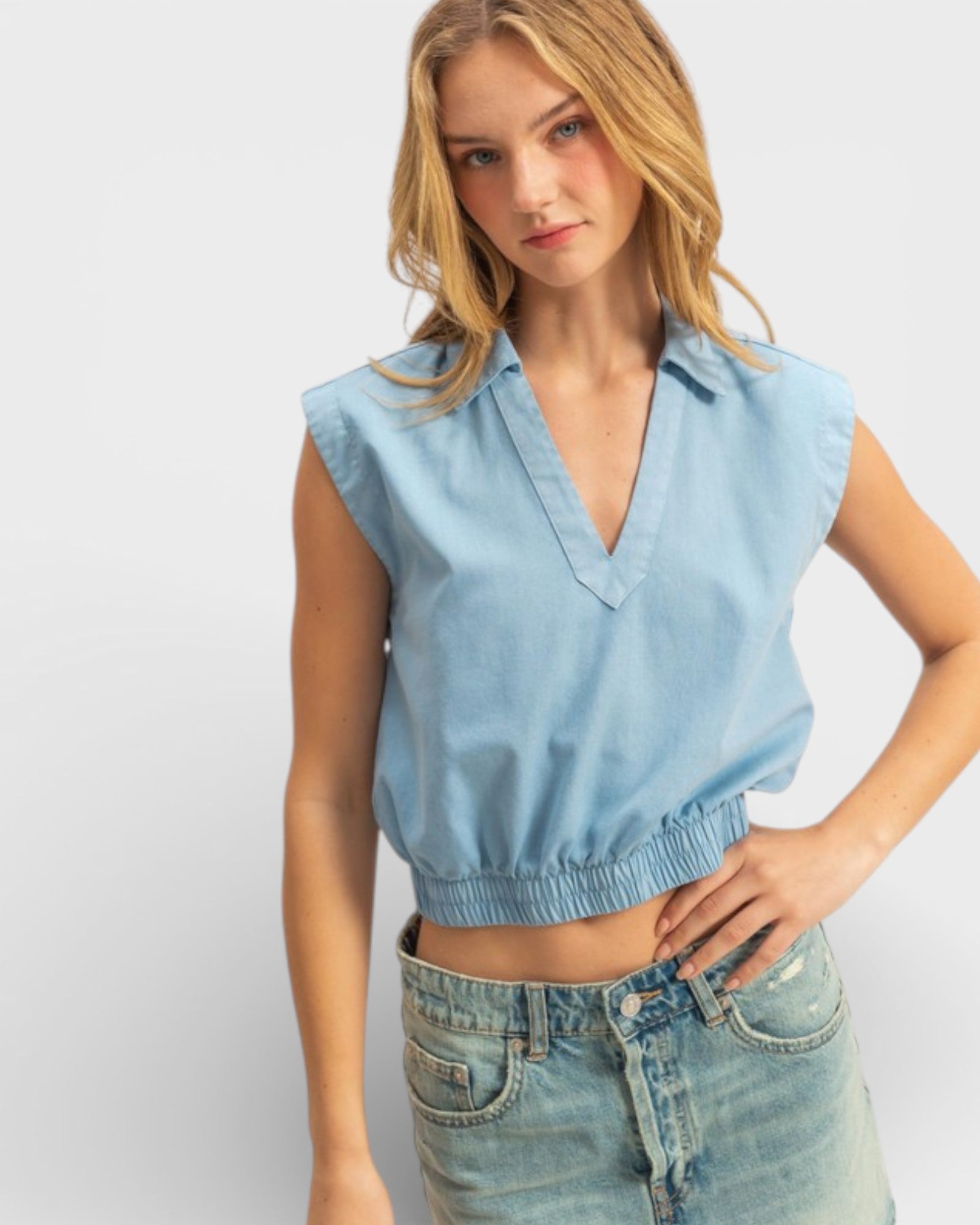 Woman wearing a light blue sleeveless top and denim shorts on a white background