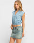 Woman wearing a light blue sleeveless denim top and matching denim skirt on a white background
