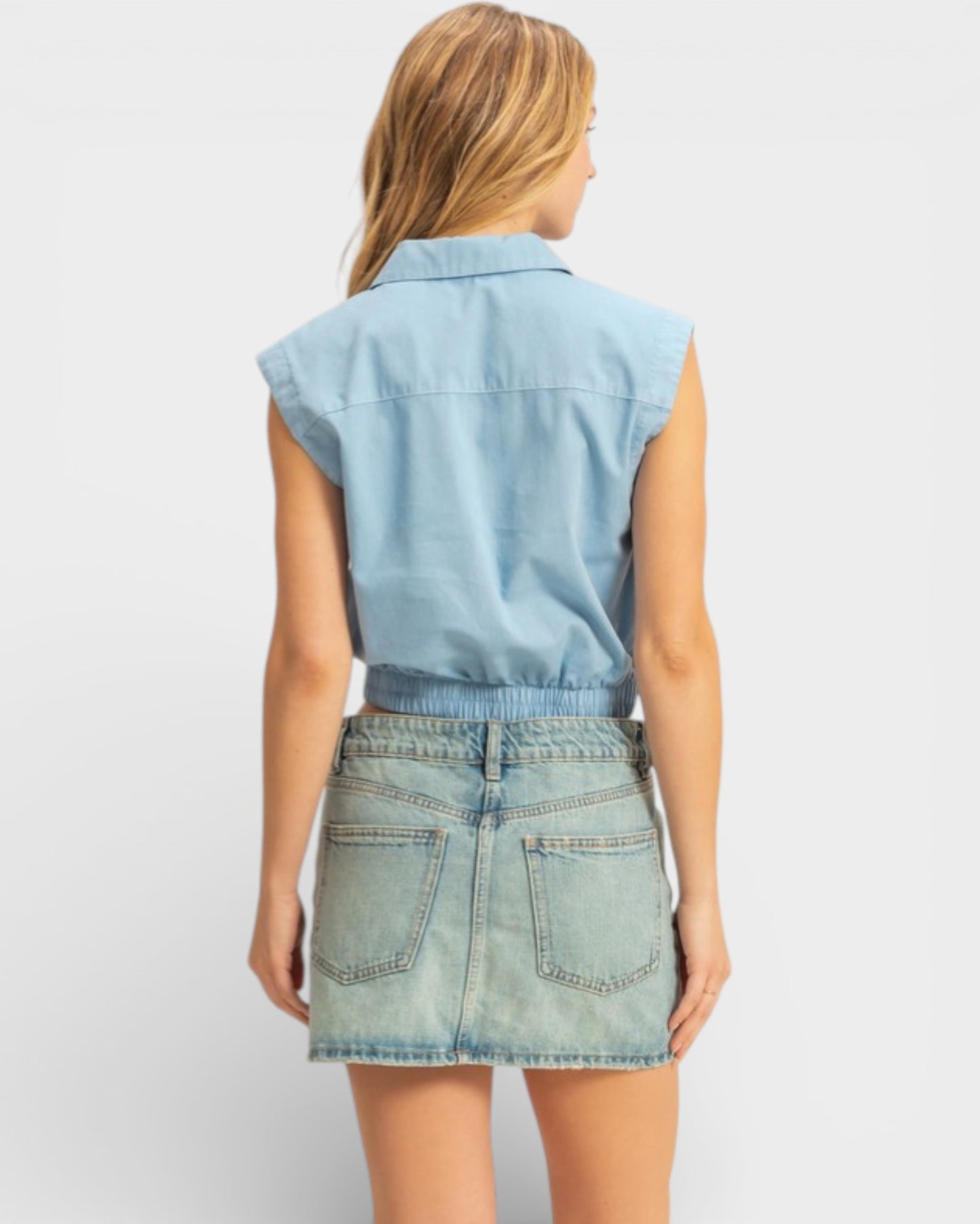 Woman wearing a light blue denim sleeveless top and skirt on a white background