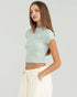 Woman wearing a light green crop top and white pants on a plain background
