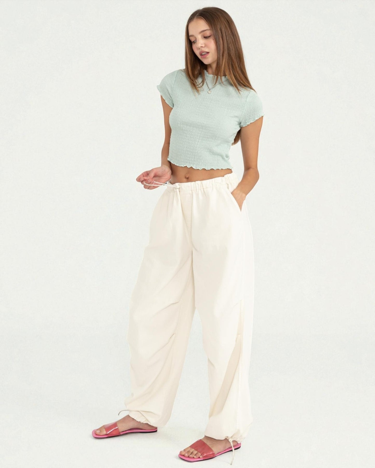 Woman wearing a light green top and white pants on a plain background