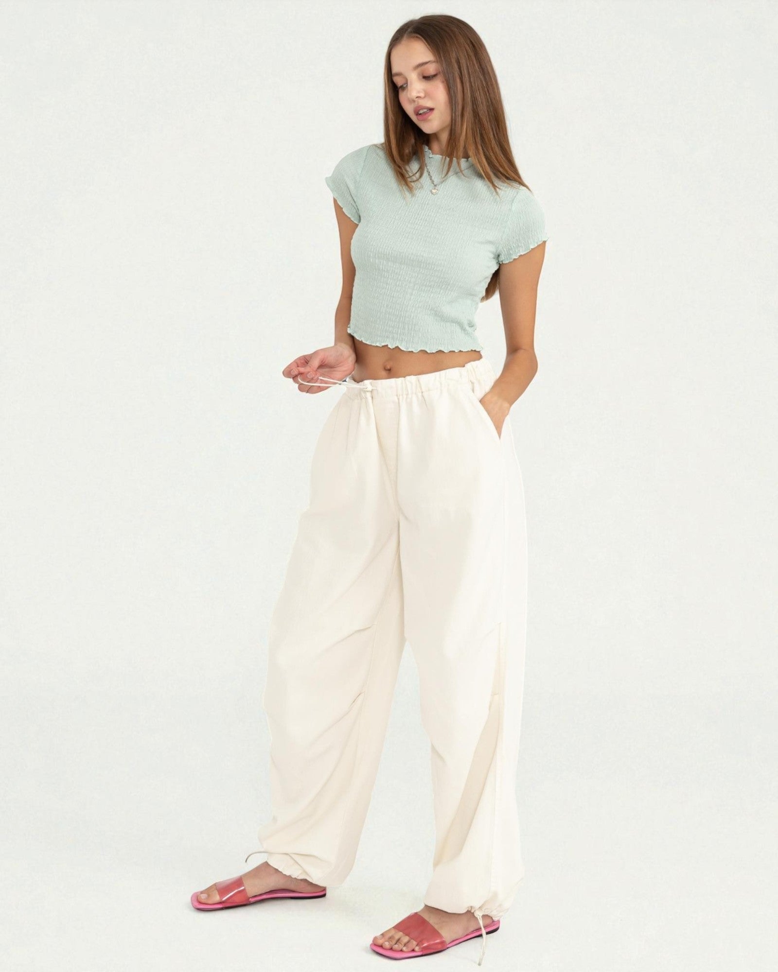 Woman wearing a light green top and white pants on a plain background