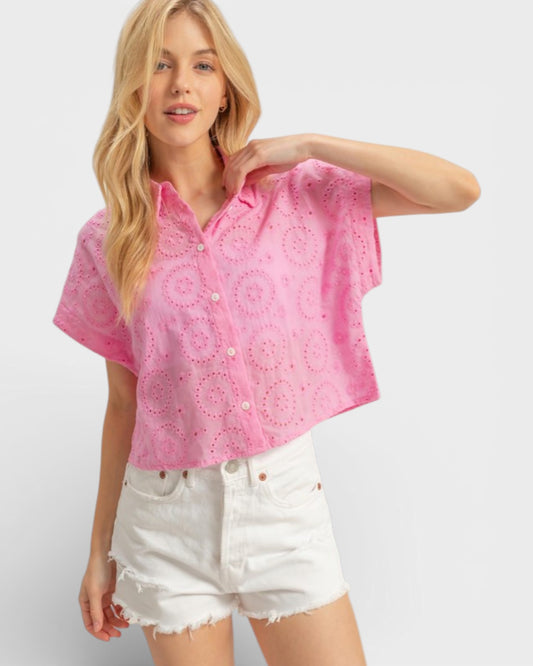 Woman wearing a pink patterned blouse and white shorts on a light gray background