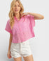 Woman wearing a pink patterned blouse and white shorts on a light gray background