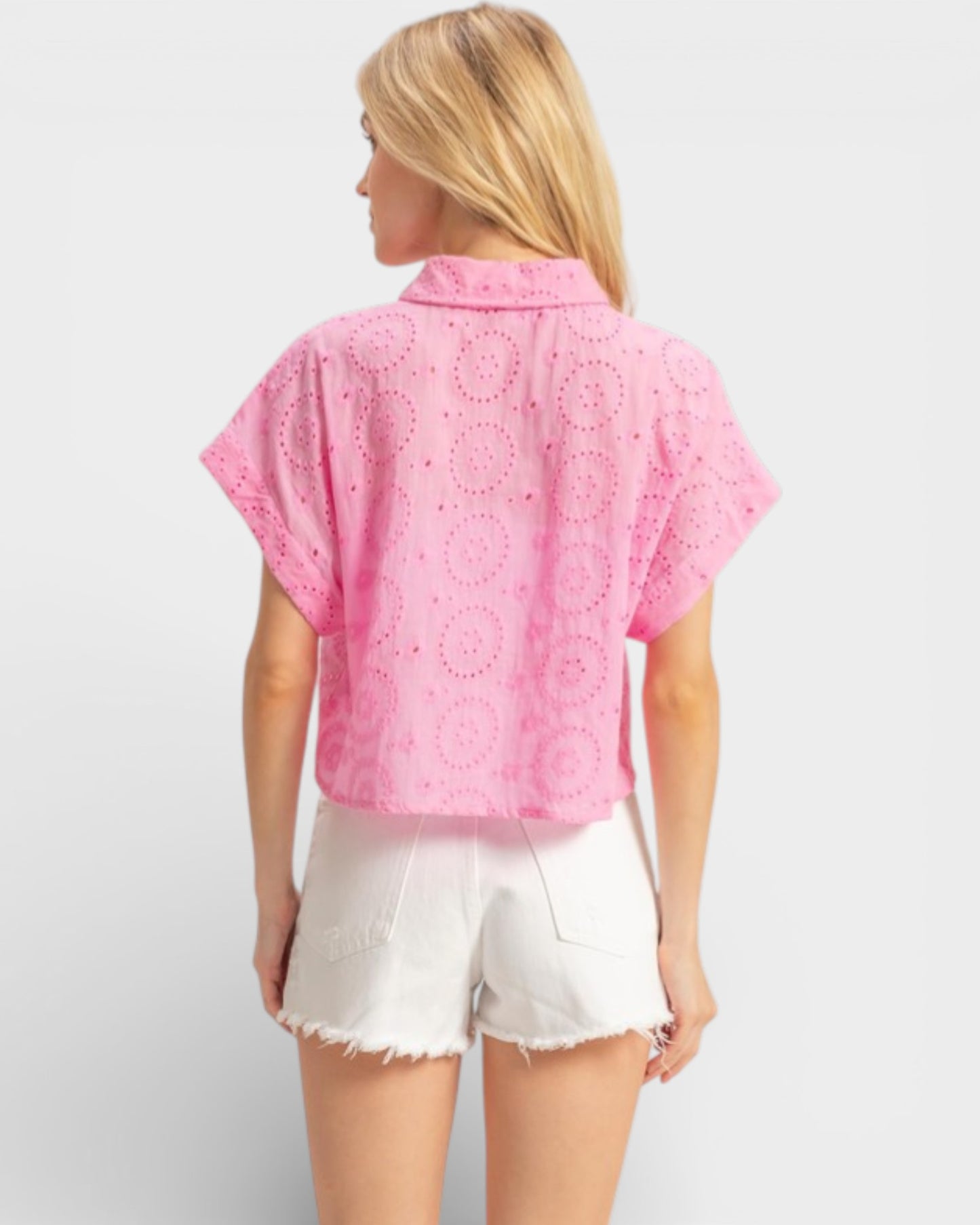 Woman wearing a pink lace top and white shorts on a light gray background