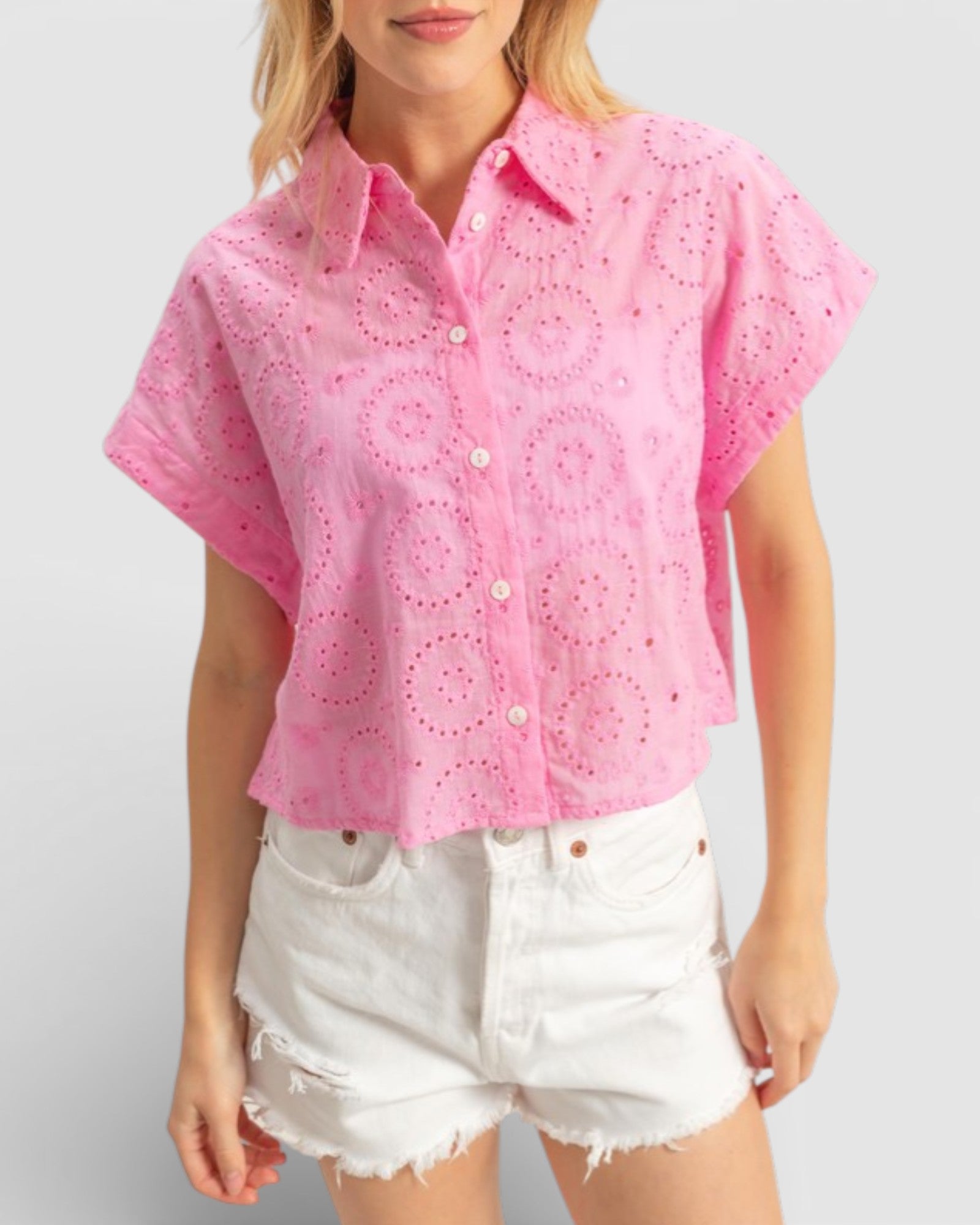 Woman wearing a pink embroidered blouse and white shorts on a plain background