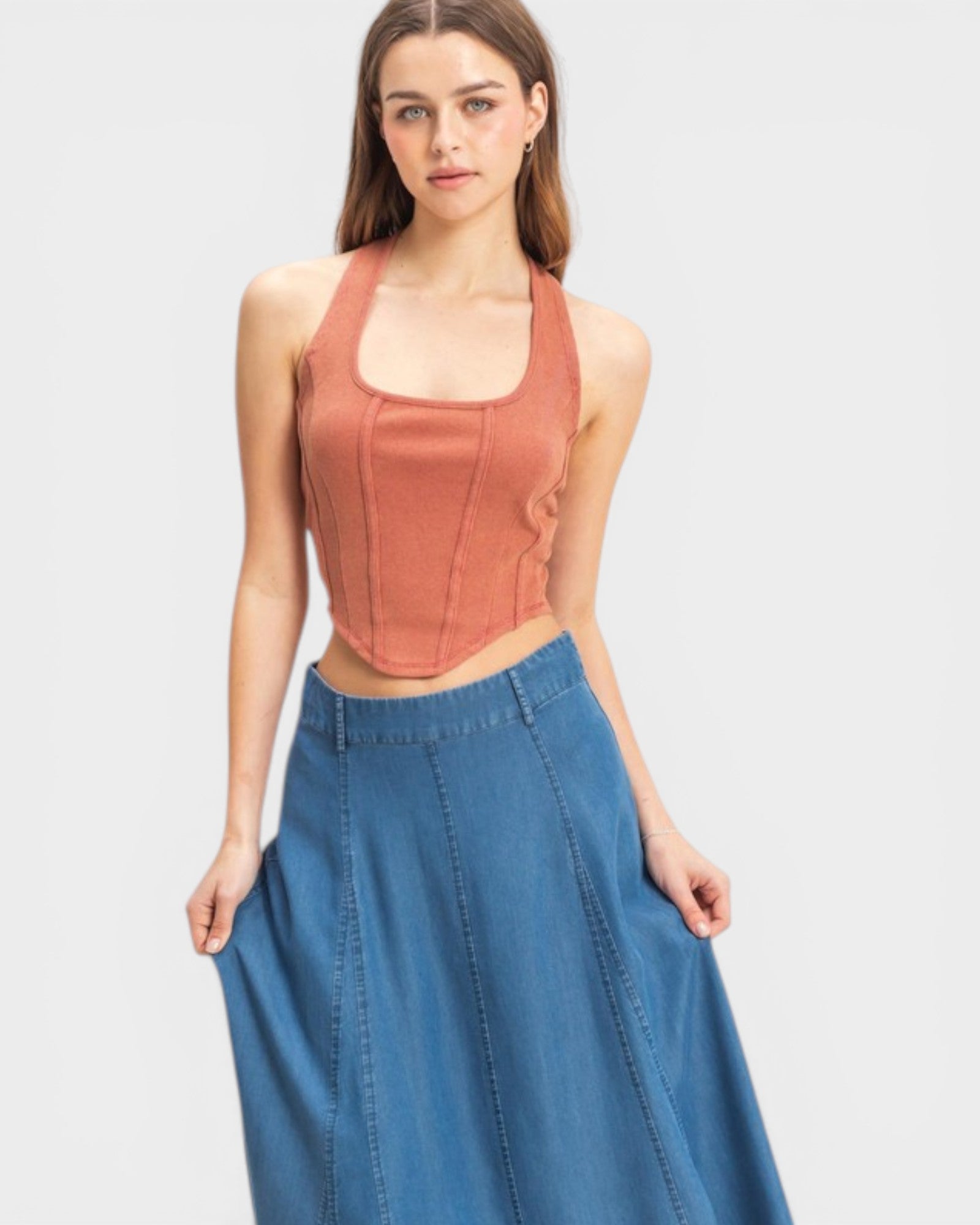 Woman wearing a rust-colored halter top and blue denim skirt on a light gray background