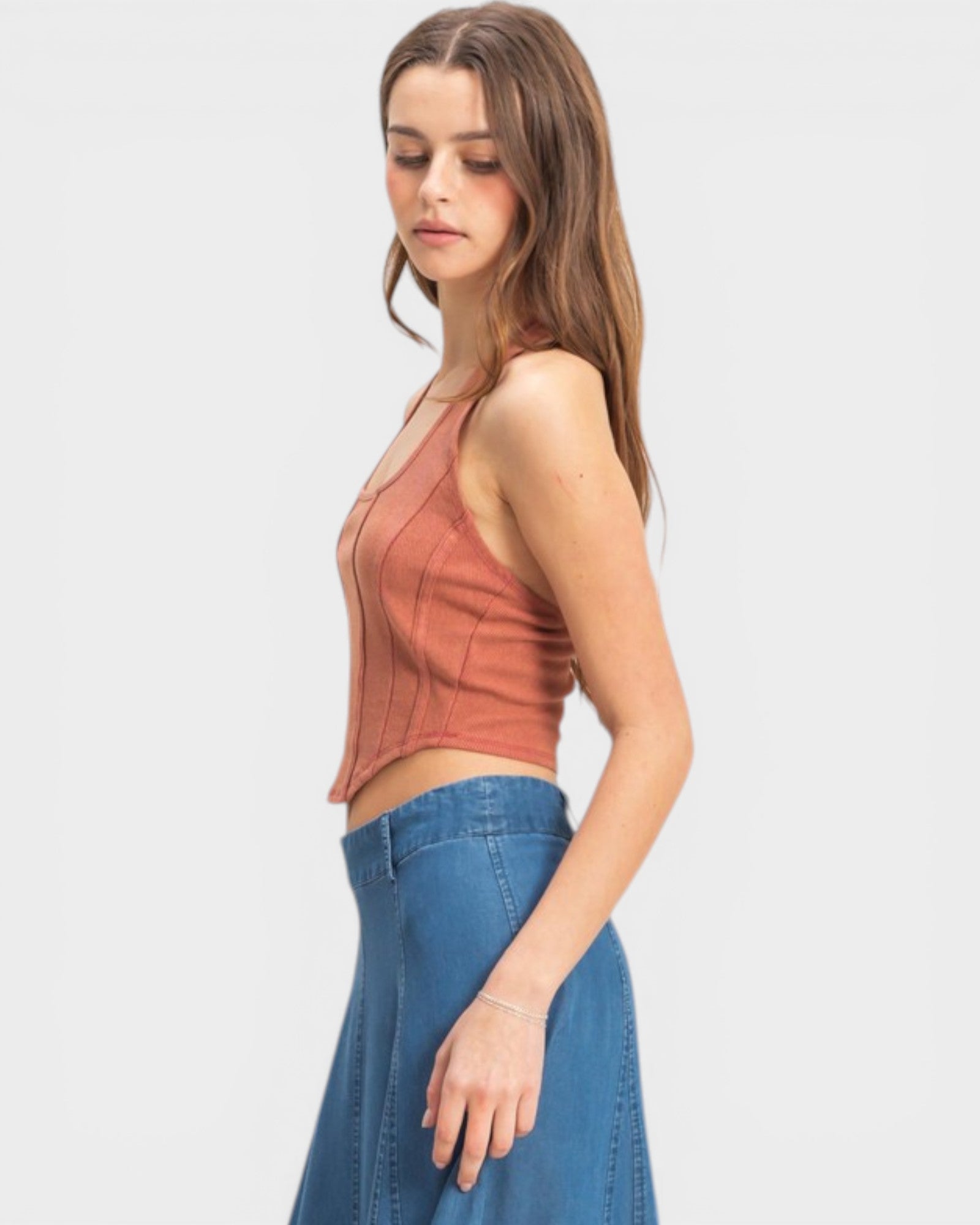 Woman wearing a rust-colored sleeveless top and blue jeans on a white background