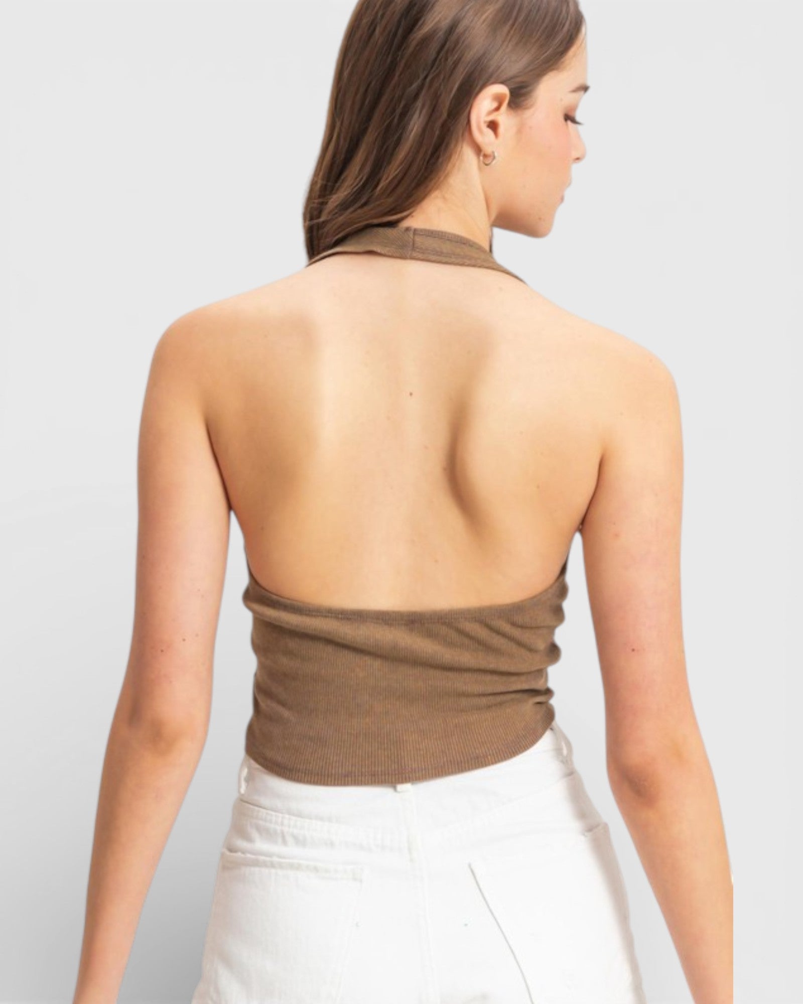 Woman wearing a brown halter top and white pants on a light gray background