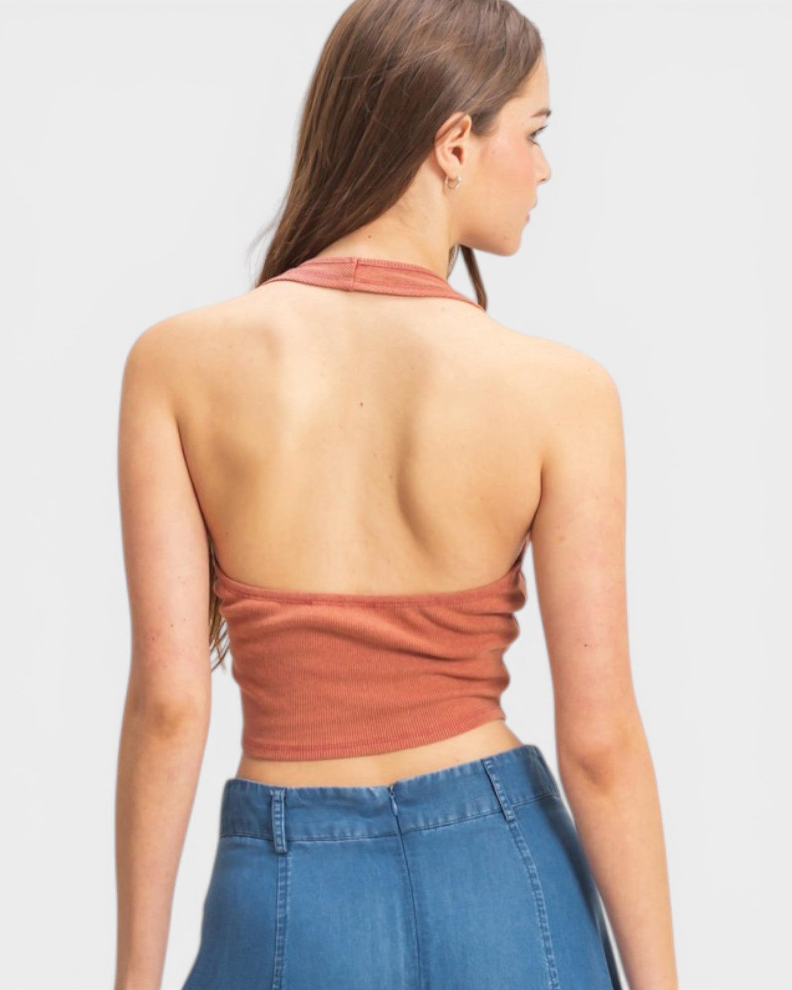 Woman wearing a rust-colored halter top and blue jeans on a light gray background