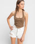 Woman wearing a brown halter top and white shorts on a light gray background