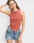 Woman wearing a rust-colored tank top and denim shorts on a white background