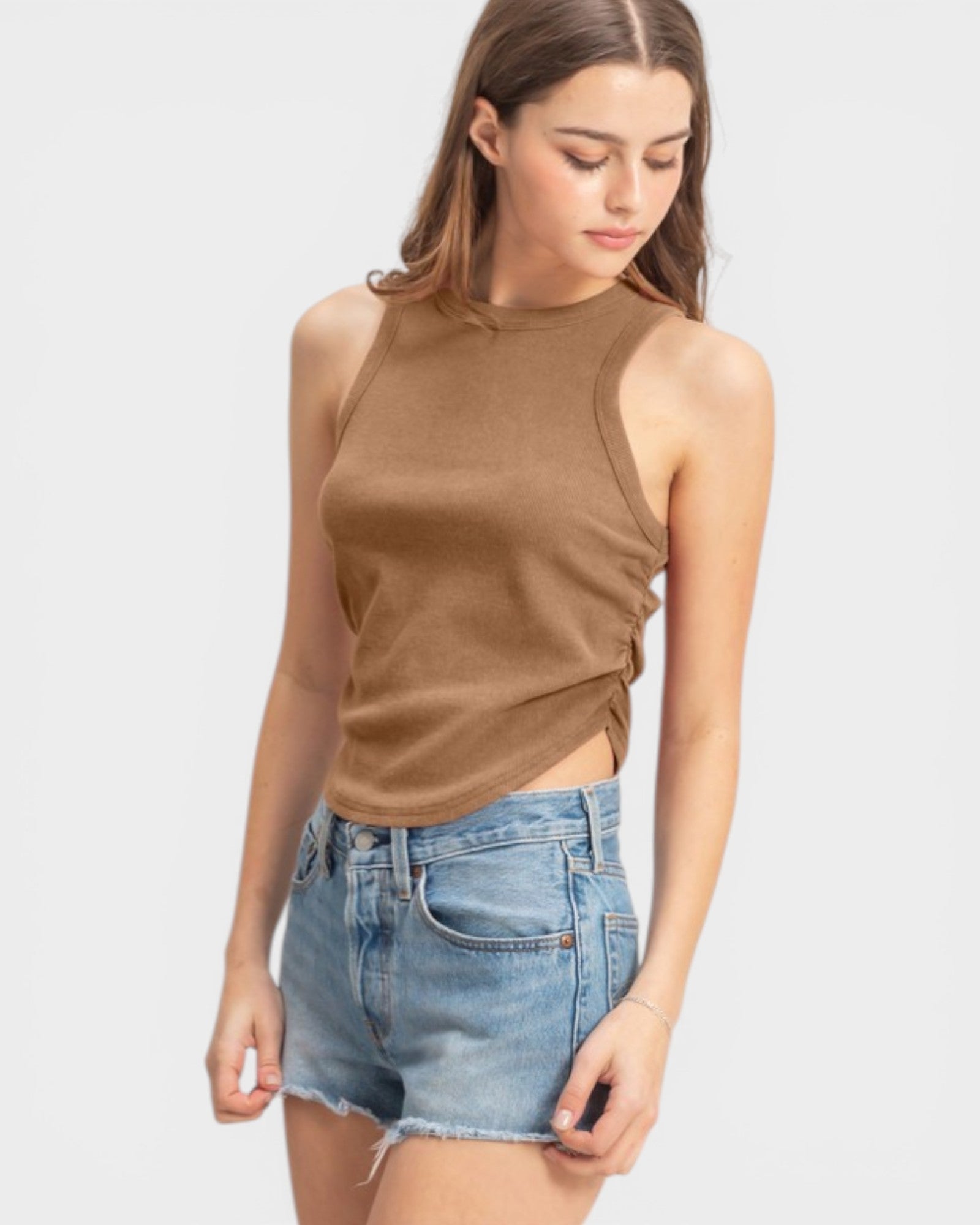 Woman wearing a brown sleeveless top and denim shorts on a white background