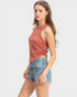Woman wearing a rust-colored sleeveless top and denim shorts on a white background