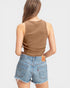 Woman wearing a brown tank top and denim shorts on a light gray background