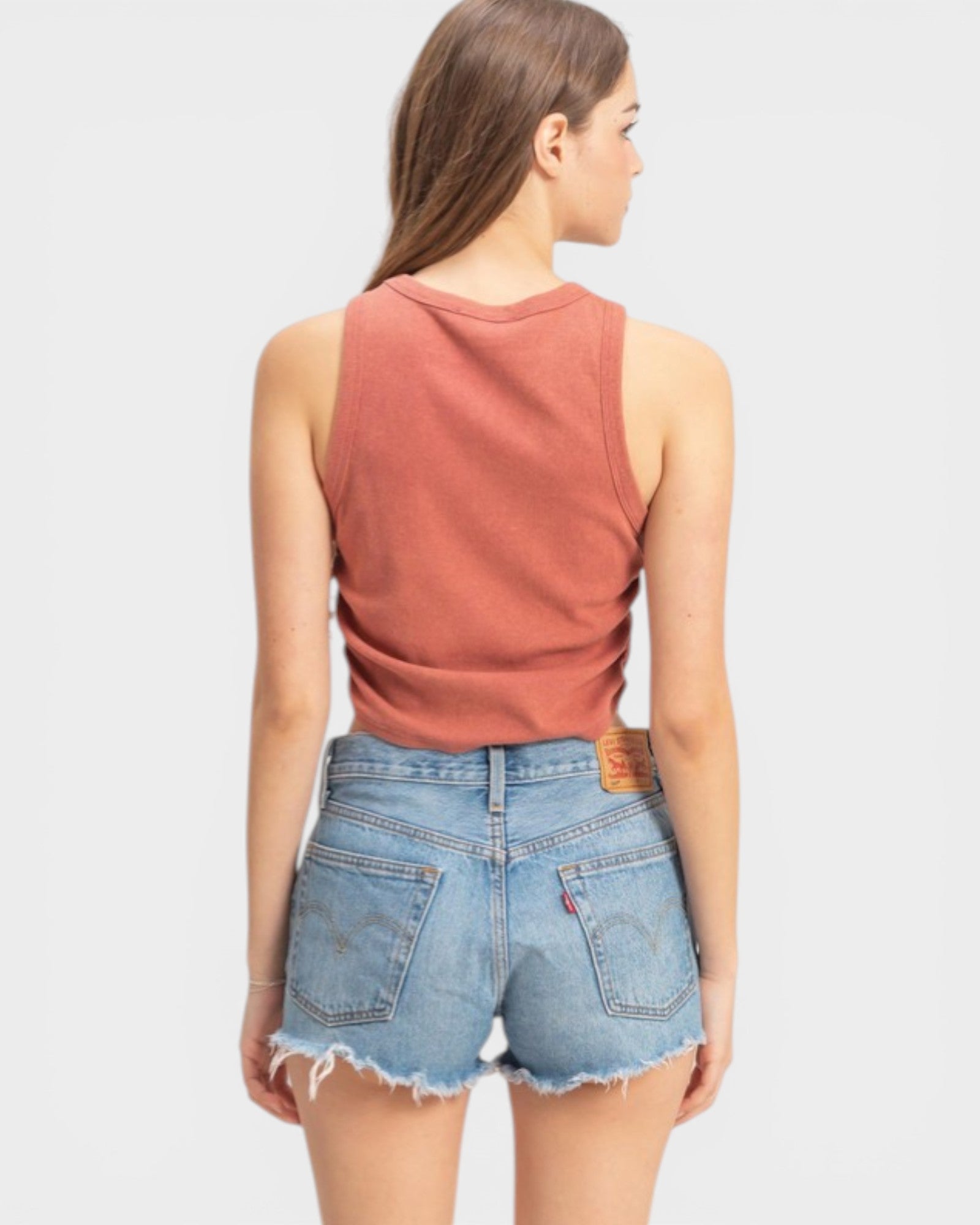 Woman wearing a rust-colored tank top and denim shorts on a light gray background