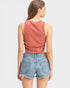 Woman wearing a rust-colored tank top and denim shorts on a light gray background