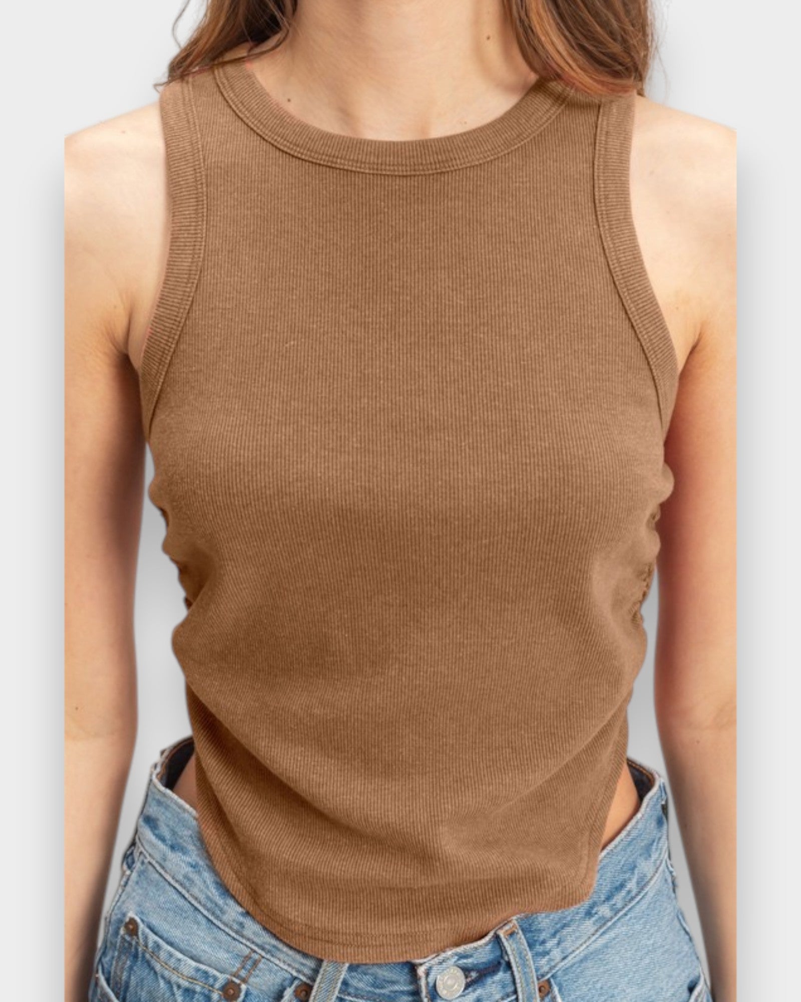 Person wearing a brown ribbed tank top and blue jeans on a light gray background