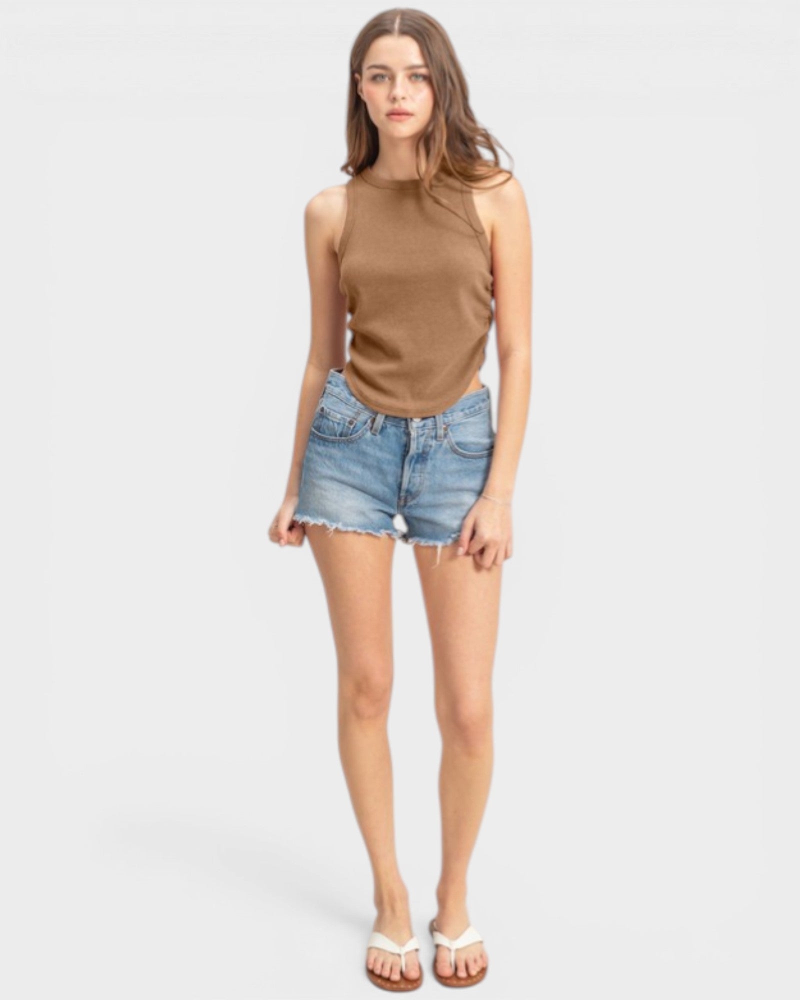 Woman wearing a brown sleeveless top and denim shorts on a white background