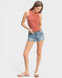 Woman wearing a sleeveless rust-colored top and denim shorts on a white background