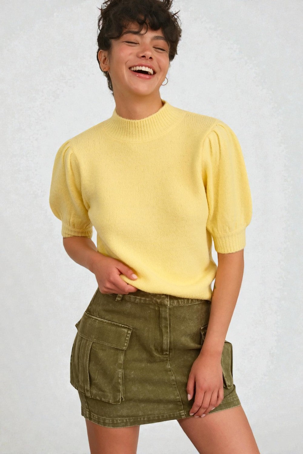 Person wearing a yellow sweater and green skirt on a white background