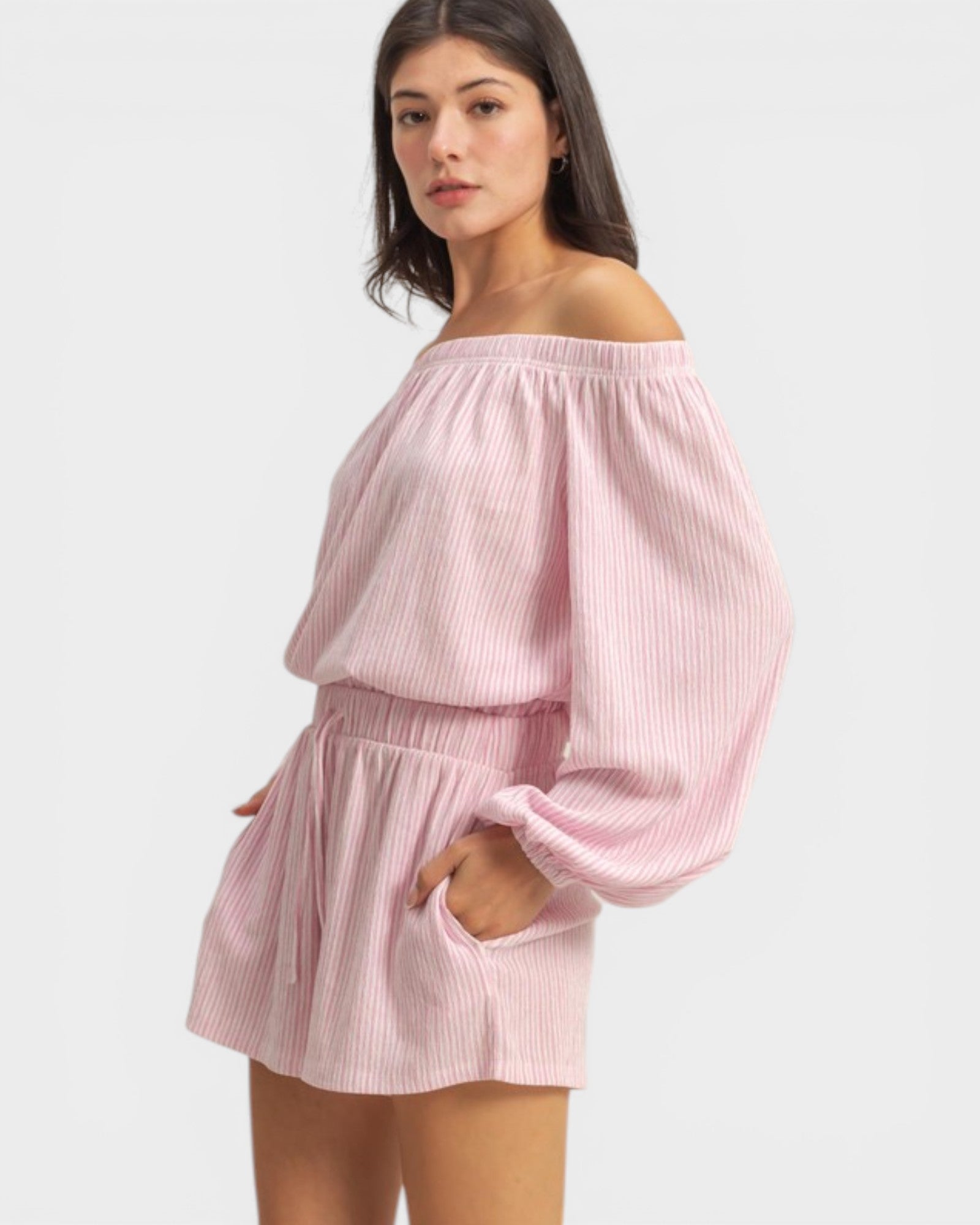 Woman wearing a pink off-shoulder top and shorts set on a white background