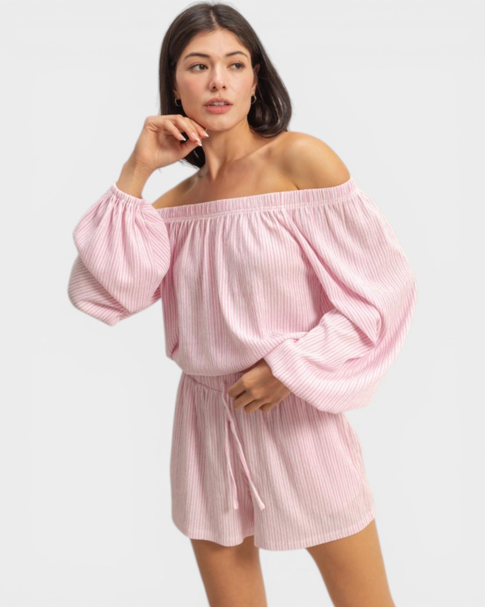 Woman wearing a pink off-shoulder top and shorts set on a white background
