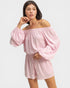 Woman wearing a pink off-shoulder top and shorts set on a white background