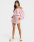 Woman wearing a pink off-shoulder top and shorts on a white background
