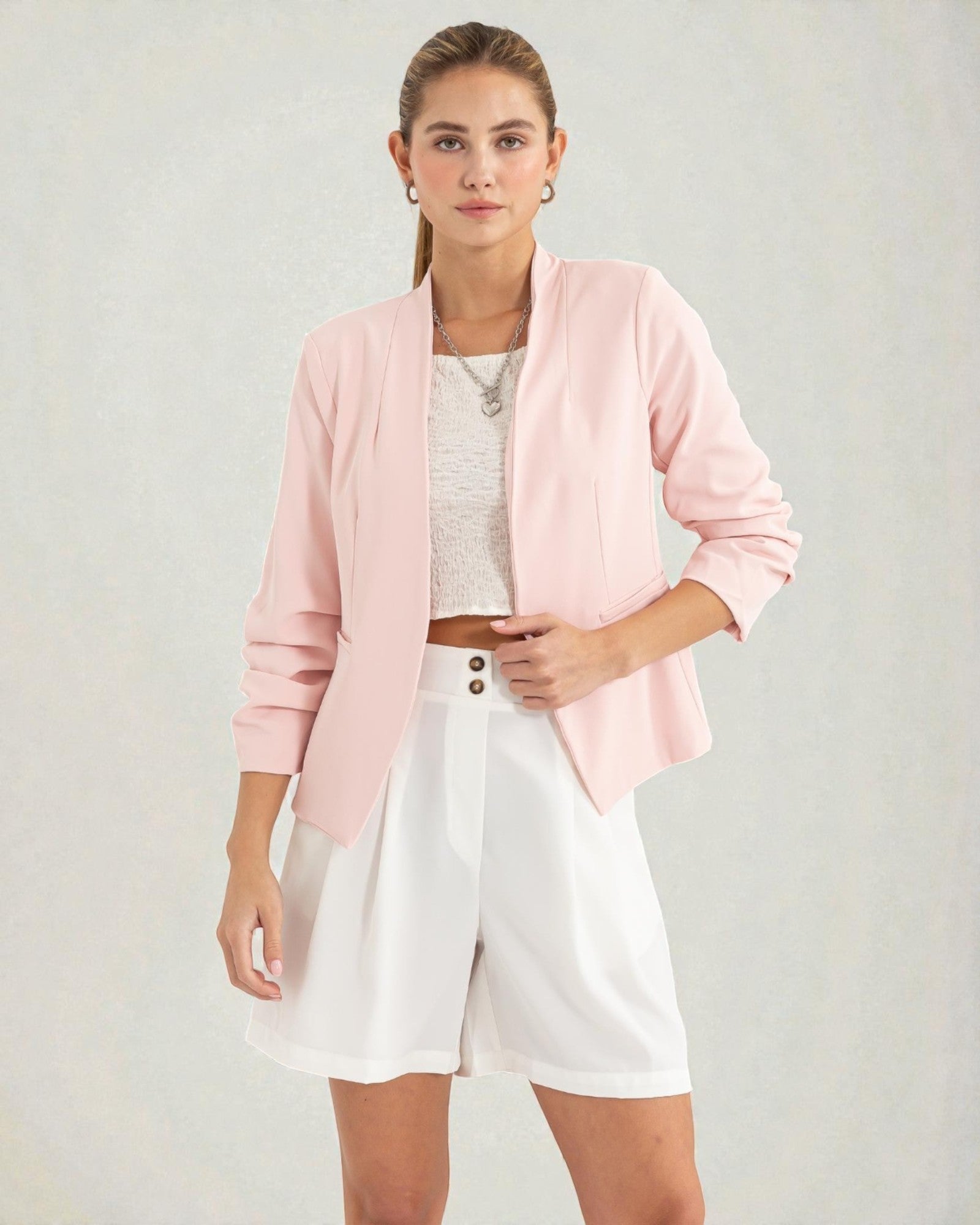 Woman wearing a pink cardigan, white top, and shorts on a plain background