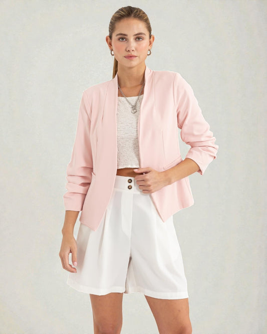 Woman wearing a pink cardigan, white top, and shorts on a plain background